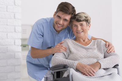 Male nurse hugging his senior woman patient sitting on a wheelchair
